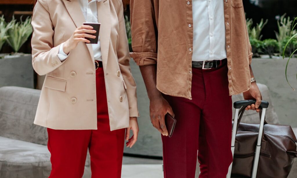 Stylish individuals in beige and burgundy outfits holding a suitcase and coffee cup indoors.